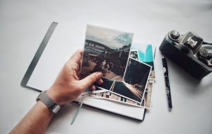 A person holding photos with a vintage camera and notebook on a desk.